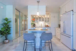 A modern kitchen with a central island, two bar stools, white cabinets, and a refrigerator.