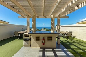 An outdoor patio with a barbecue area, seating, and a view of the ocean. - Kamaole Beach Royale 206 1 Bedroom Condo (Kihei)