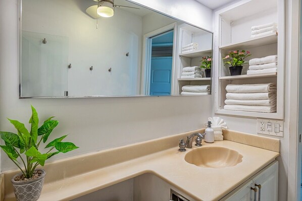 A bathroom with a beige sink, a mirror, and shelves with folded towels.