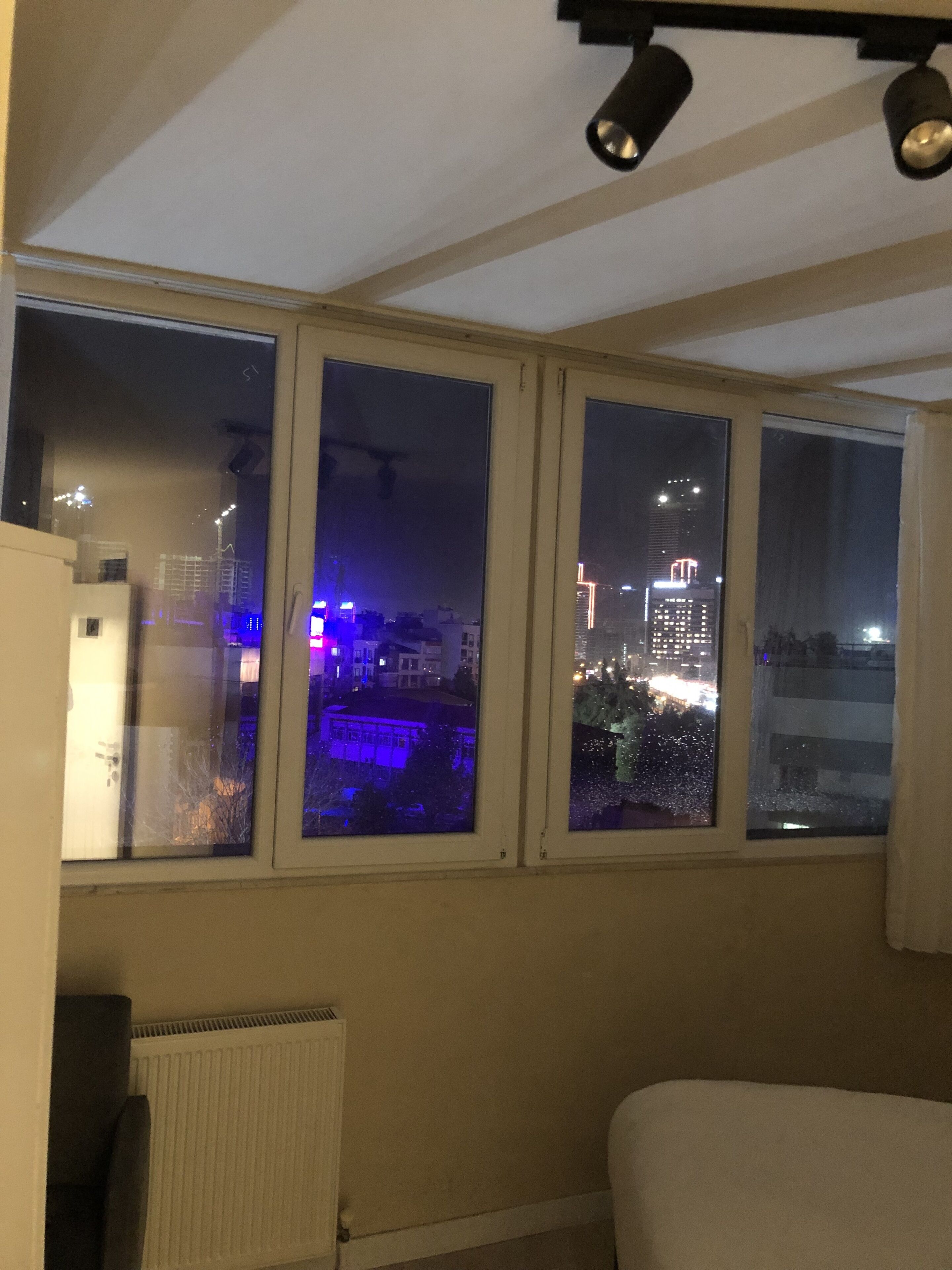 A room with a large window overlooking a cityscape at night.
