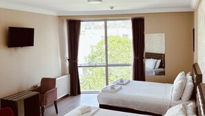 A hotel room with two beds, a desk, a chair, a TV, and a large window with curtains. - Punta Vista Otel (Izmir)