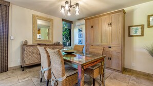 A dining area with a glass-top table, wicker chairs, a wooden cabinet, and a ceiling light fixture. - Wailea Ekahi, #33b 1 Bedroom Condo by RedAwning (Kihei)
