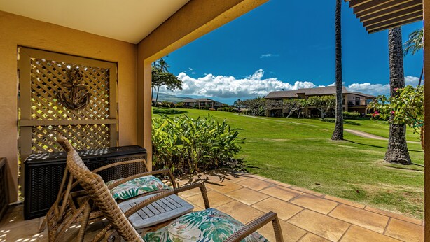 A covered outdoor seating area with wicker furniture and a view of a well-maintained lawn and buildings in the distance. - Wailea Ekahi, #33b 1 Bedroom Condo by RedAwning (Kihei)