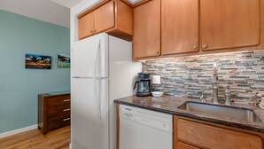 A kitchen with wooden cabinets, a white refrigerator, a coffee maker, and a tiled backsplash. - Kihei Surfside, #508 1 Bedroom Condo by RedAwning (Kihei)