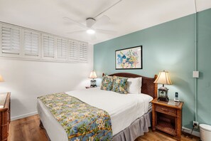 A hotel room with a bed, two bedside tables, a ceiling fan, a wall-mounted picture, and a window with blinds. - Kihei Surfside, #508 1 Bedroom Condo by RedAwning (Kihei)
