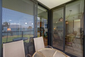 A modern interior with a glass door leading to an outdoor area, furnished with chairs and a table. - Kihei Surfside, #508 1 Bedroom Condo by RedAwning (Kihei)