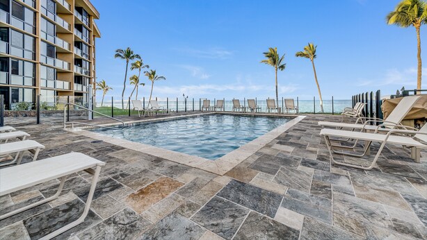 A pool area with lounge chairs and palm trees, overlooking a body of water. - Kihei Surfside, #508 1 Bedroom Condo by RedAwning (Kihei)