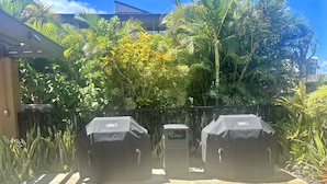 A patio area with two Weber barbecue grills, surrounded by lush greenery and a tiled floor. - Wailea Elua, #0908 2 Bedroom Condo by RedAwning (Kihei)