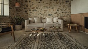 Un salon chaleureux avec un mur en pierre, un canapé, une table basse et un petit tabouret.