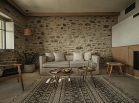 Una sala de estar acogedora con pared de piedra, un sofá, una mesita de centro y un taburete pequeño.