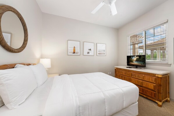 A bedroom with a bed, a wooden dresser, a television, and three framed pictures on the wall.