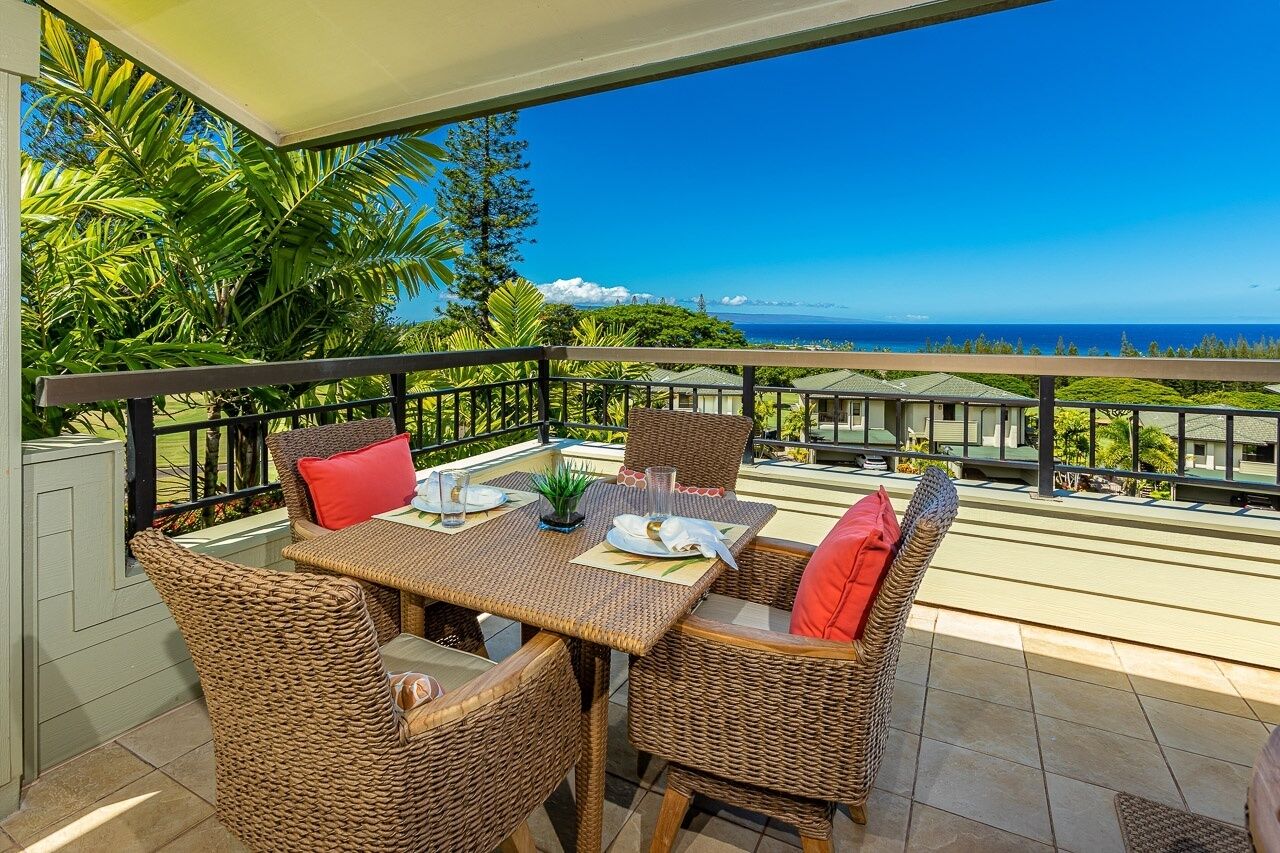 Uma varanda com móveis de vime, uma mesa posta com pratos e copos, e vista para o mar.