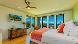 A bedroom with a large bed, a ceiling fan, a TV on the wall, and a view of the ocean through large windows. - Kapalua Golf Villas by Coldwell Banker Island Vacations (Lahaina)