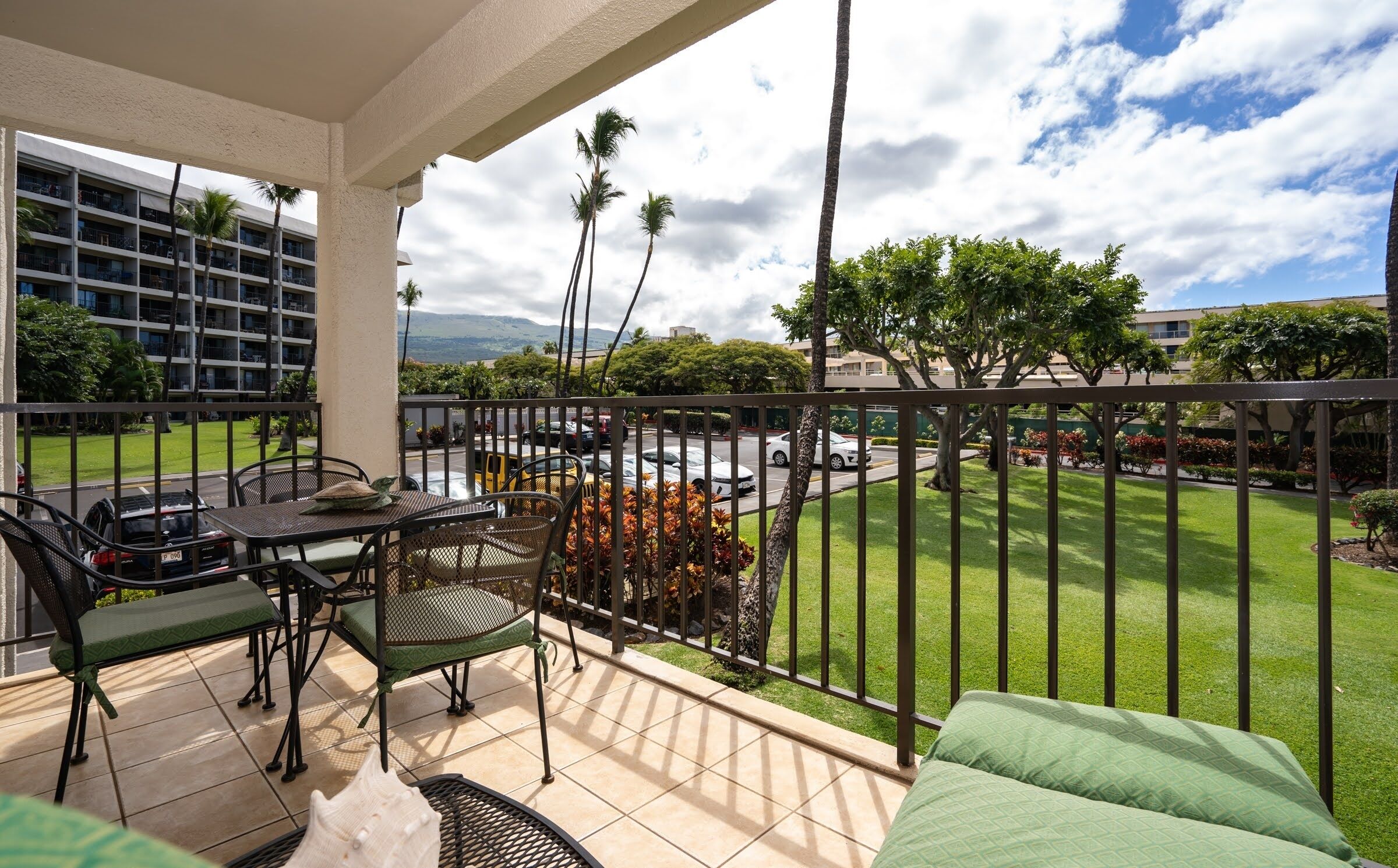 A balcony with a view of a parking area, a building, and a grassy area with trees.