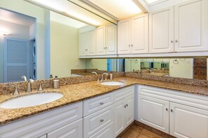 Une salle de bain avec deux lavabos, des meubles blancs, un grand miroir et un comptoir en granit.