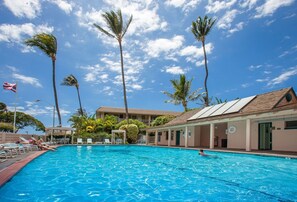 Ein Swimmingpool mit Liegestühlen und Palmen, umgeben von Gebäuden mit einem Ziegeldach.
