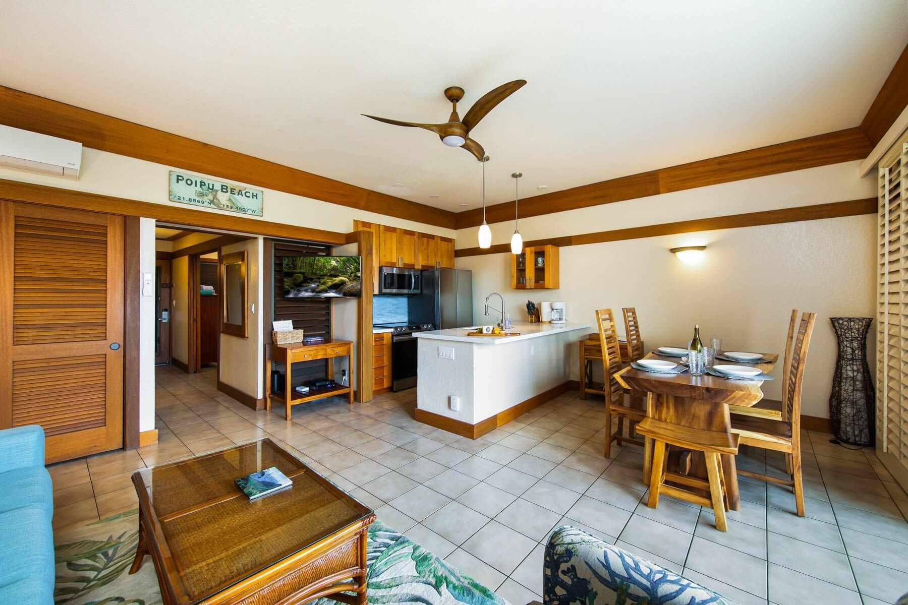 A spacious living area with a dining table, wooden chairs, a TV, and a kitchen area with a microwave and refrigerator.