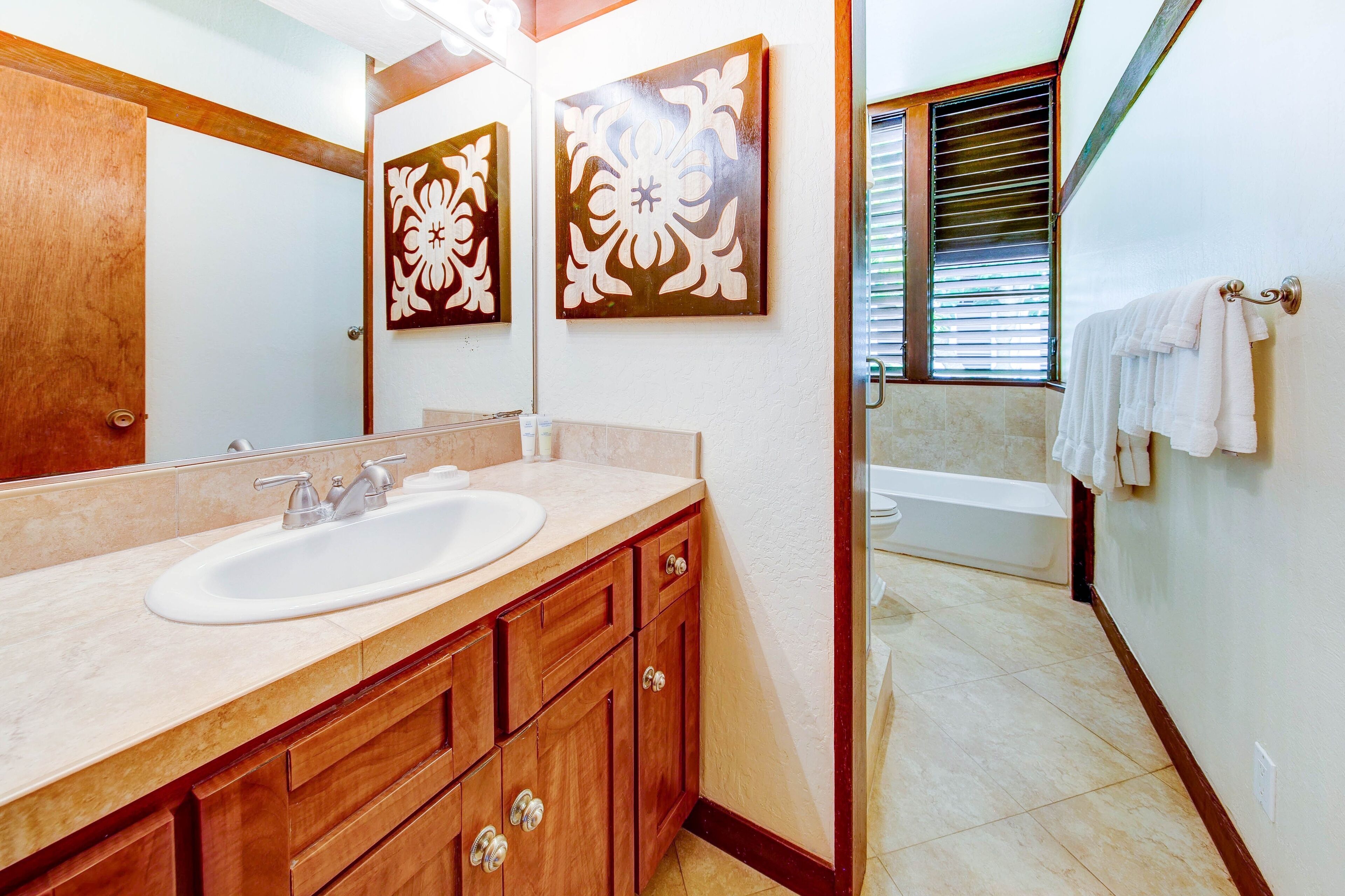 A bathroom with a sink, mirror, wooden cabinets, and a bathtub.