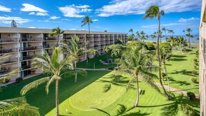 A multi-story hotel with a pool area, palm trees, and a view of the ocean. - Maui Sunset A504 1 Bedroom Condo (Kihei)