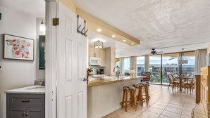 A kitchen with a white countertop, wooden stools, and a view of the balcony. - Maui Sunset A504 1 Bedroom Condo (Kihei)