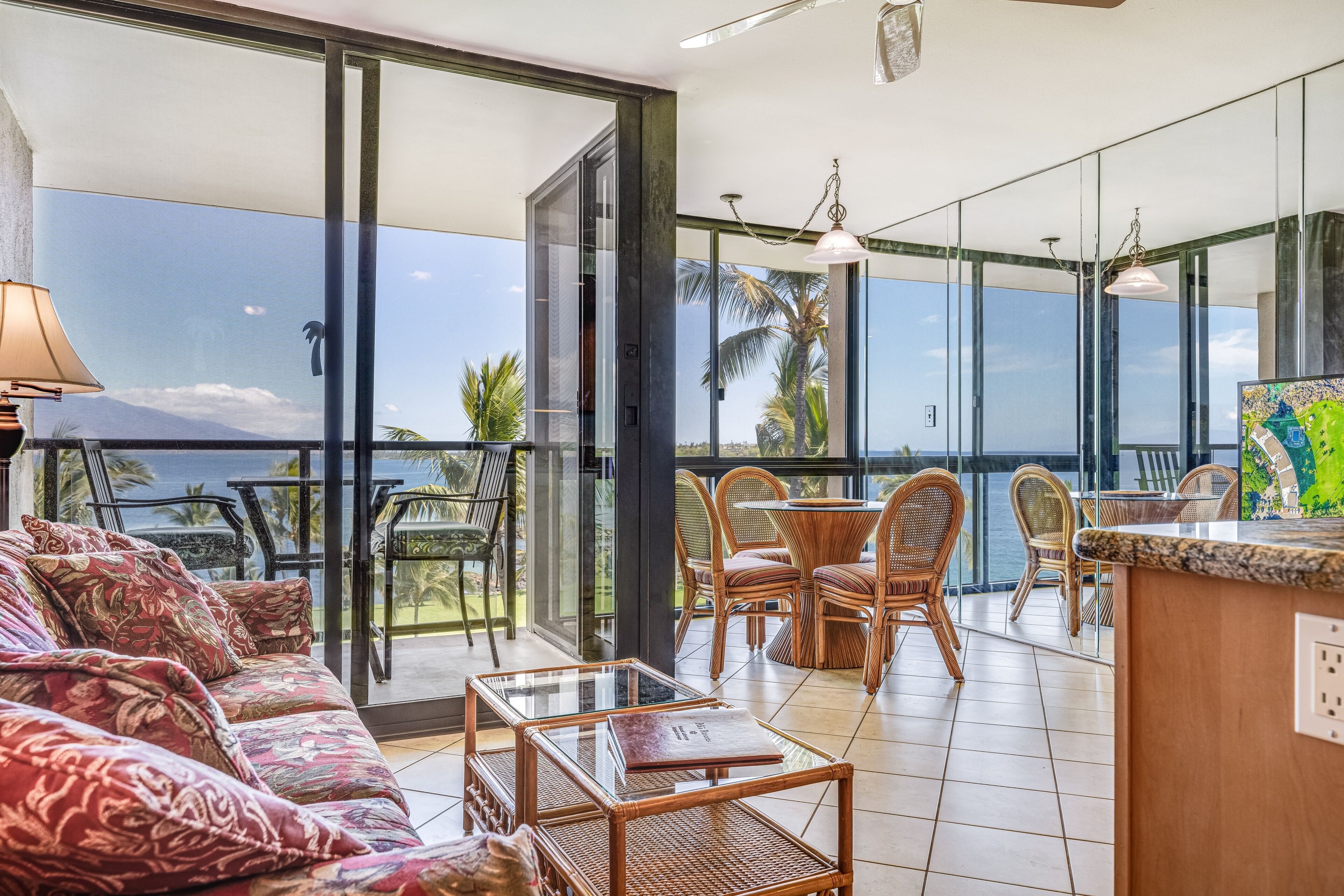 A balcony with a glass door, wicker furniture, and a view of the ocean.