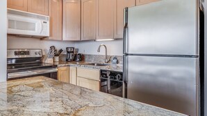 A modern kitchen with stainless steel appliances, wooden cabinets, and granite countertops. - Kihei Surfside, #609 1 Bedroom Condo by RedAwning (Kihei)
