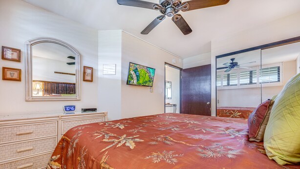 A bedroom with a bed, a dresser, a mirror, a ceiling fan, and a painting on the wall. - Kihei Surfside, #609 1 Bedroom Condo by RedAwning (Kihei)