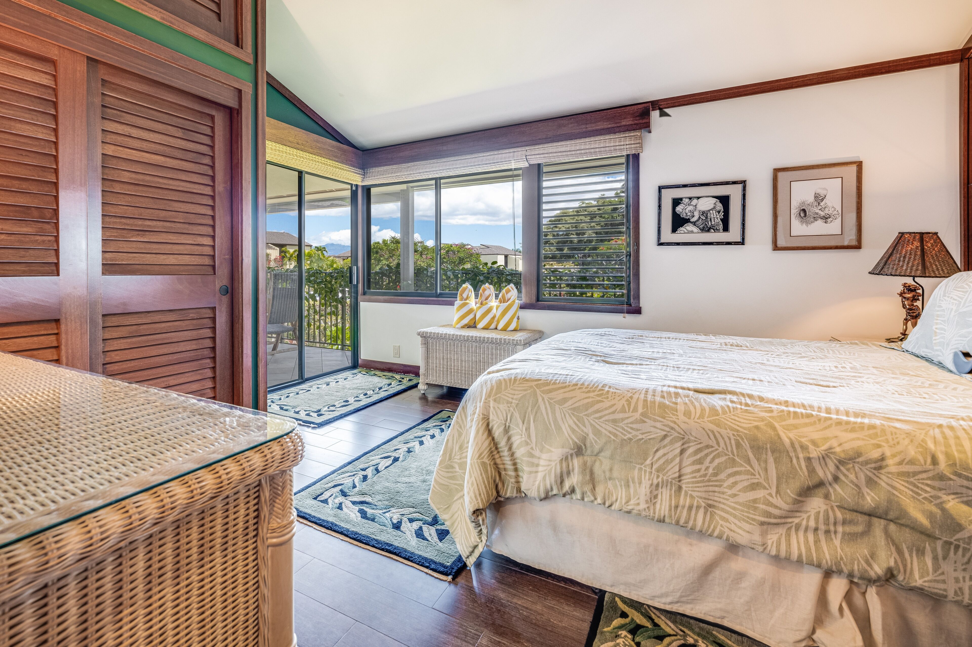 A bedroom with a large bed, a wicker chair, a small table, and a view of the outdoors through a sliding door.