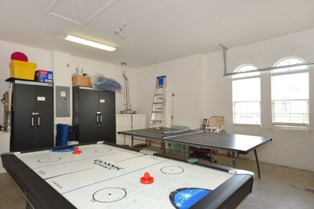 A room with an air hockey table, two black cabinets, a ladder, and a window with blinds.