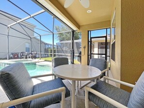 Un patio techado con piscina, mobiliario exterior y vistas al jardín trasero.