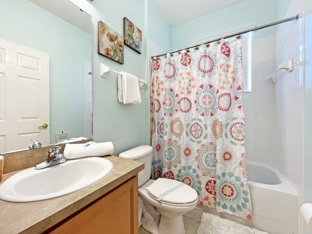 A bathroom with a white sink, toilet, and bathtub. There is a patterned shower curtain and a towel rack with a towel.