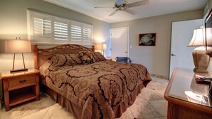 A bedroom with a bed, two bedside tables, a ceiling fan, a window with blinds, and a door.