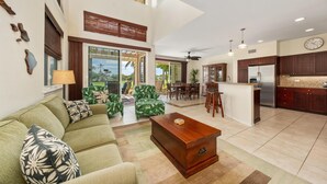 A spacious living area with a green sofa, a wooden coffee table, and a dining area with a kitchen in the background. - Big Island Fairway Villas by Coldwell Banker Island Vacations (Waikoloa)