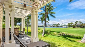 A covered outdoor seating area with lounge chairs and a view of a golf course and ocean. - Big Island Fairway Villas by Coldwell Banker Island Vacations (Waikoloa)