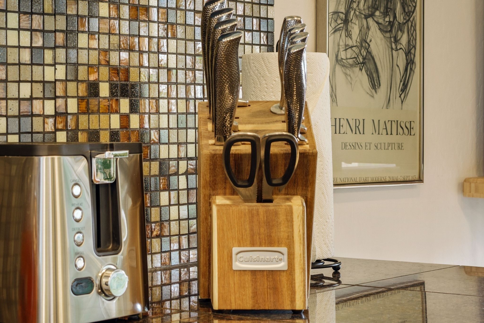 A kitchen with a toaster, a wooden knife block, and a framed artwork of Henri Matisse.