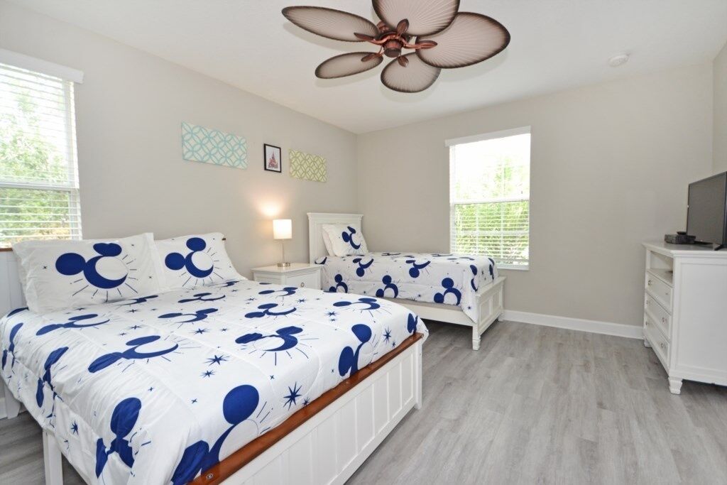 A bedroom with two beds, a ceiling fan, a TV, and a dresser.