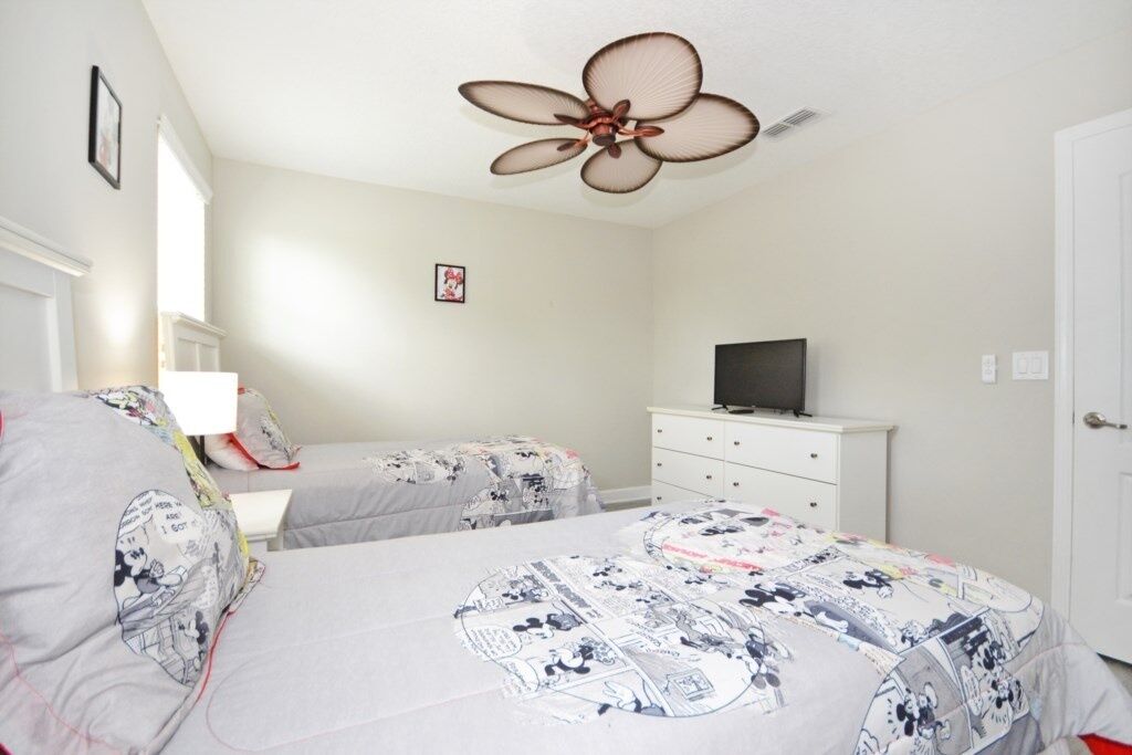 A bedroom with two beds, a ceiling fan, a TV on a dresser, and a window with blinds.