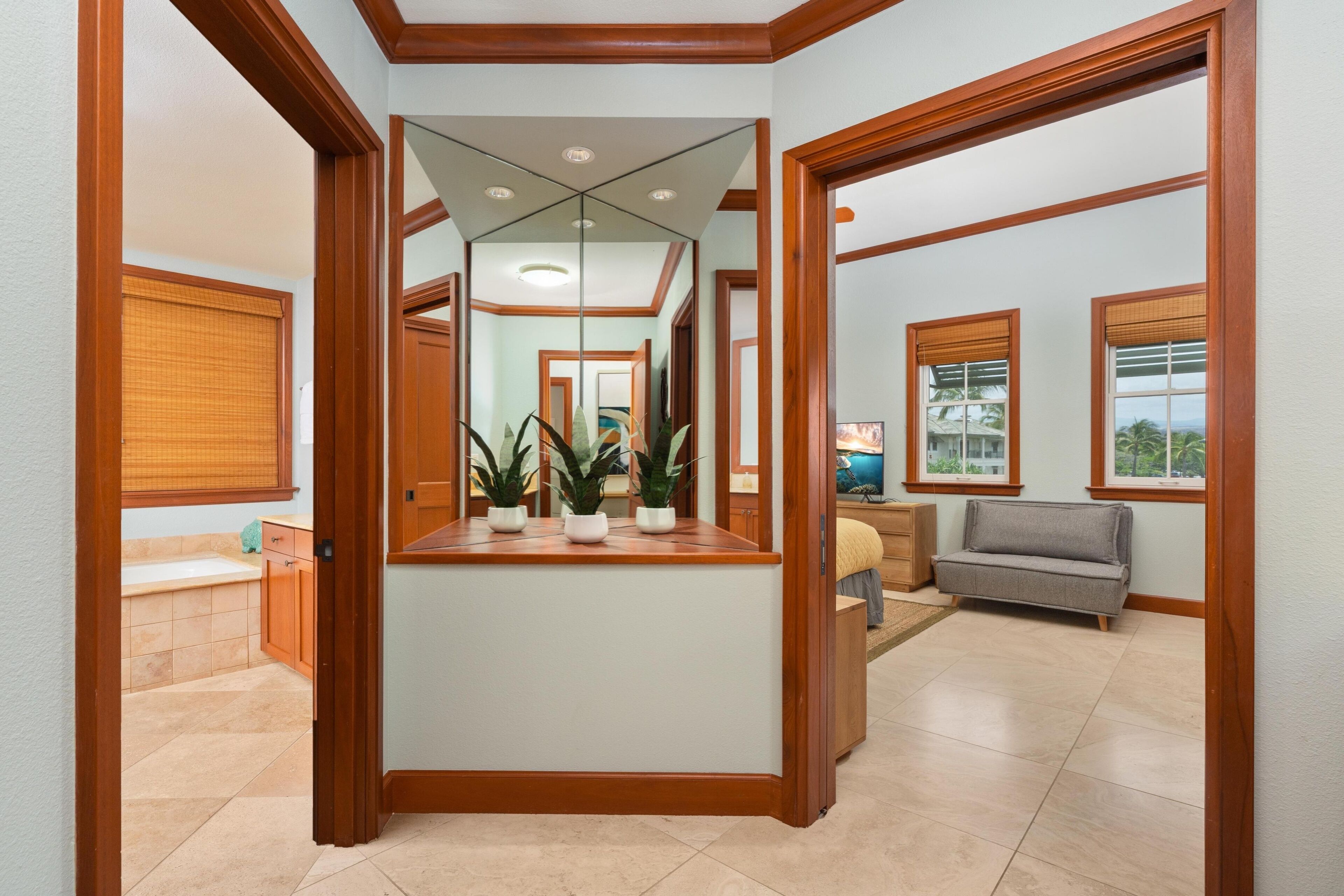 A hallway with a mirror, wooden door frames, a sofa, and a view of a bathroom.