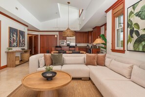 A modern living room with a sectional sofa, a round wooden coffee table, and a kitchen in the background. - Big Island Kolea by Coldwell Banker Island Vacations (Waikoloa)