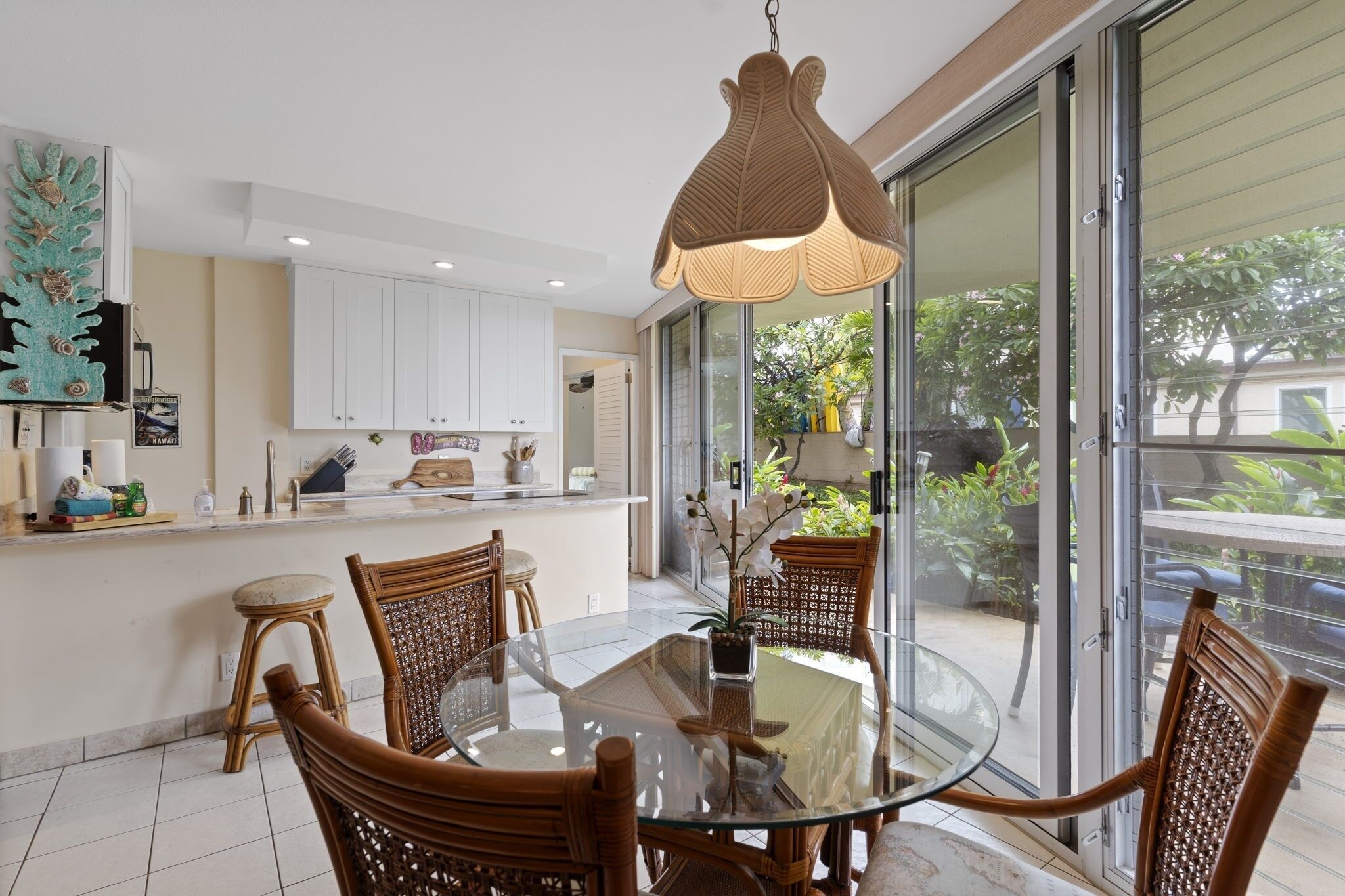 A modern kitchen with white cabinets, a glass dining table, and wicker chairs.