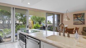 Una cocina moderna con una isla grande, puertas de cristal correderas a un balcón y vistas de un jardín tropical.