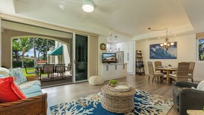 A spacious living area with a large sliding glass door leading to a patio, a dining area with wicker furniture, and a kitchen with modern appliances. - Palms at Wailea One Bedrooms by Coldwell Banker Island Vacations (Kihei)