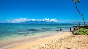 A beach with clear turquoise water, a sandy shore, and a view of distant mountains.