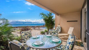 A dining area with a table set for four, overlooking a beach with a clear view of the ocean and clouds.