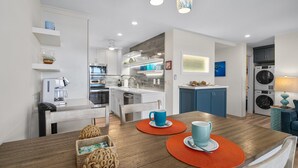 A modern kitchen with white cabinets, a dining table with orange placemats, and a blue mug on the table.