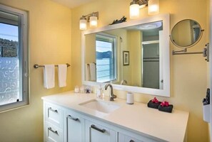 Une salle de bain avec un meuble-lavabo blanc, un grand miroir et une fenêtre donnant sur la mer.