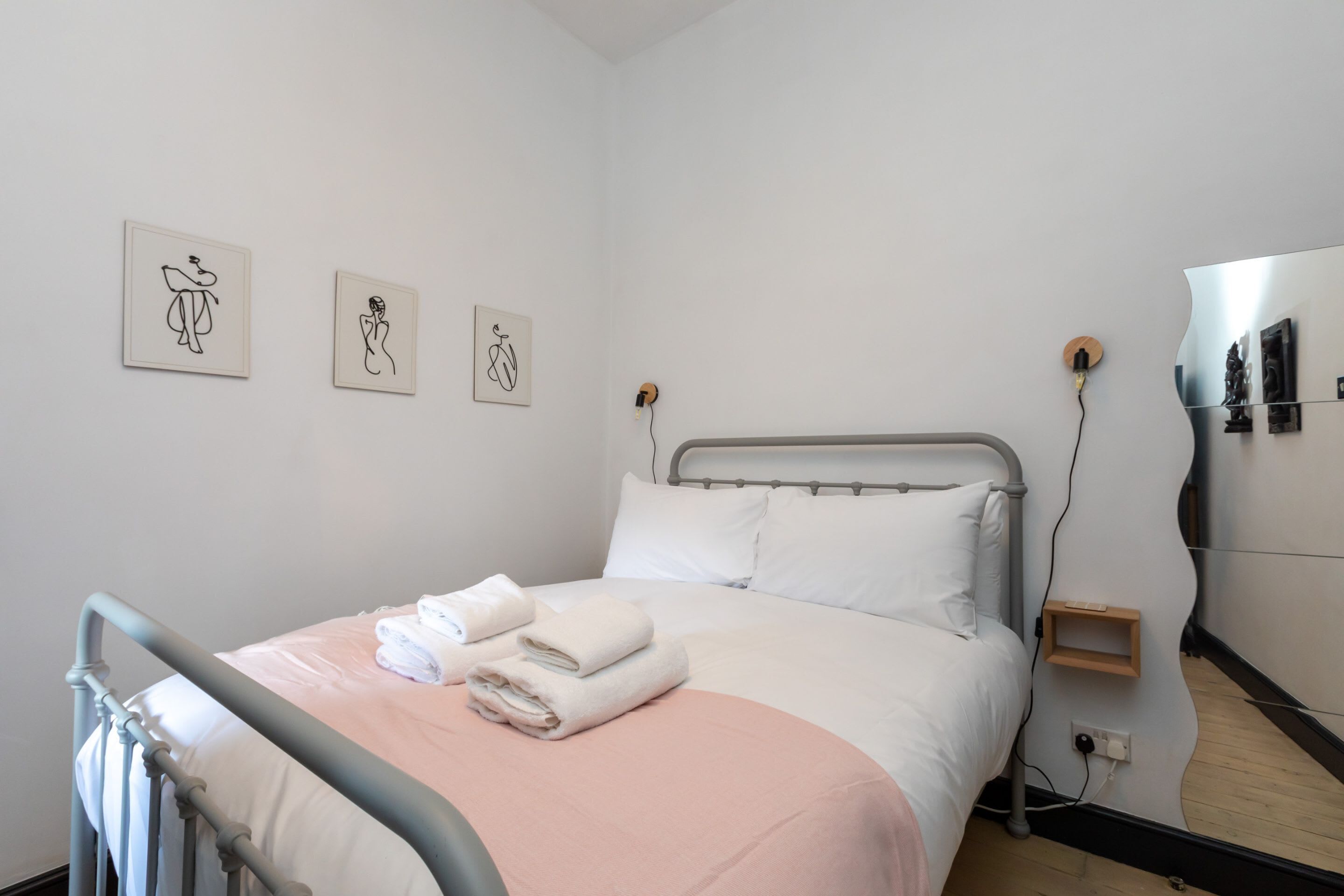 Un letto rifatto con lenzuola bianche e rosa, una testiera in metallo e due opere d'arte a parete raffiguranti figure astratte.
