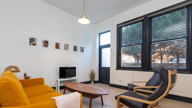 A modern living room with a yellow sofa, a wooden coffee table, a black chair, and a TV on a white stand. - Serene and Spacious 1 Bedroom Garden Flat in Clapton (London)