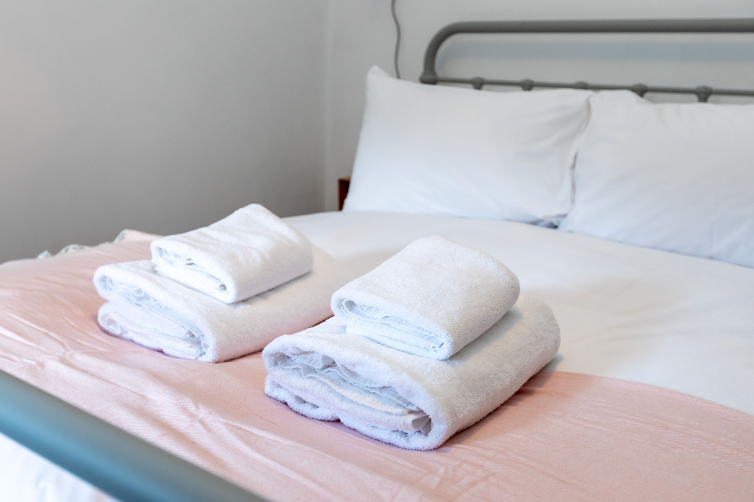 Un letto rifatto con lenzuola bianche e una coperta rosa.