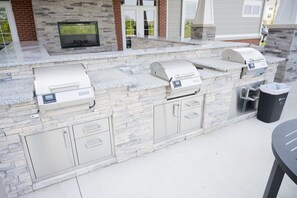 An outdoor kitchen with stone countertops, built-in grills, and a trash can.